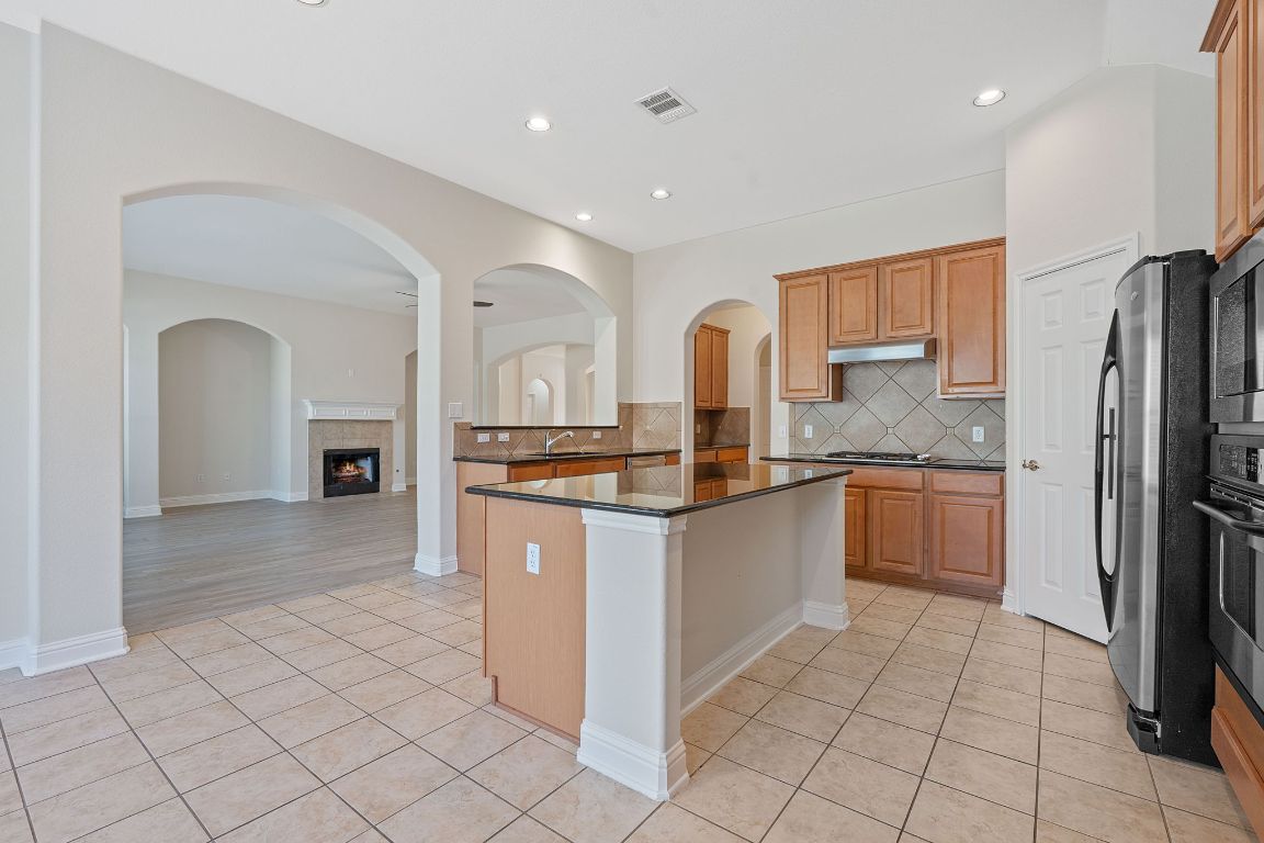 738 Nelson Ranch Road Cedar Park, TX 78613 - Photo 11 of 35 Kitchen featuring light tile patterned flooring, stainless steel appliances, a tiled fireplace, tasteful backsplash, and under cabinet range hood