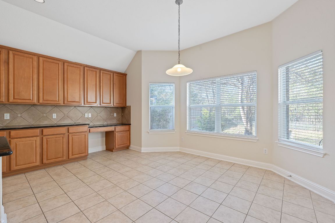 738 Nelson Ranch Road Cedar Park, TX 78613 - Photo 12 of 35 Kitchen featuring pendant lighting, lofted ceiling, dark countertops, built in desk, and decorative backsplash