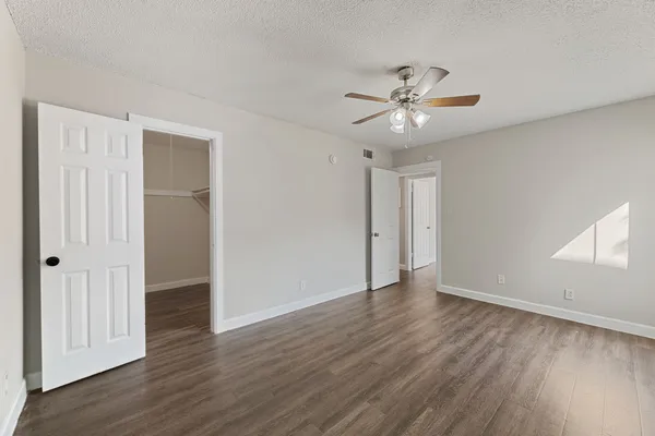 a view of an empty room with wooden floor and a ceiling fan