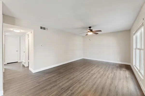 an empty room with wooden floor fan and windows