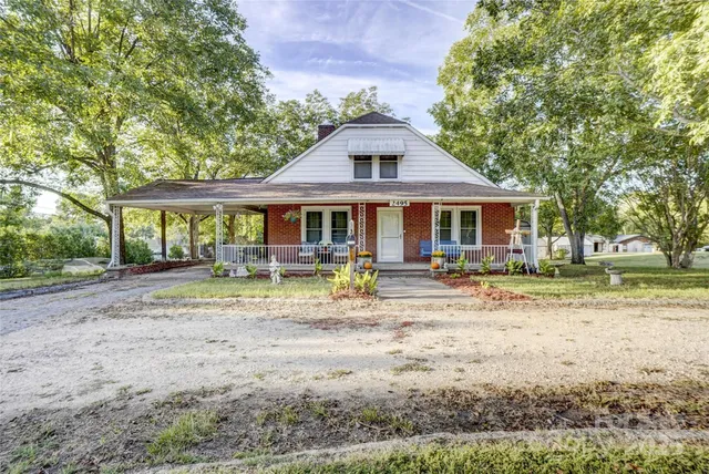 a view of a white house with a yard plants and large tree