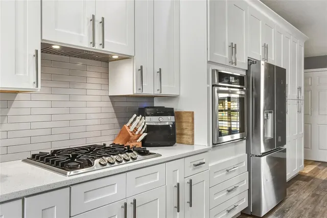 a kitchen with stainless steel appliances granite countertop a stove a refrigerator and a white cabinets