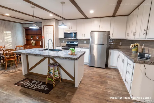 a kitchen with stainless steel appliances kitchen island granite countertop a refrigerator a stove a sink a dining table and chairs with wooden floor