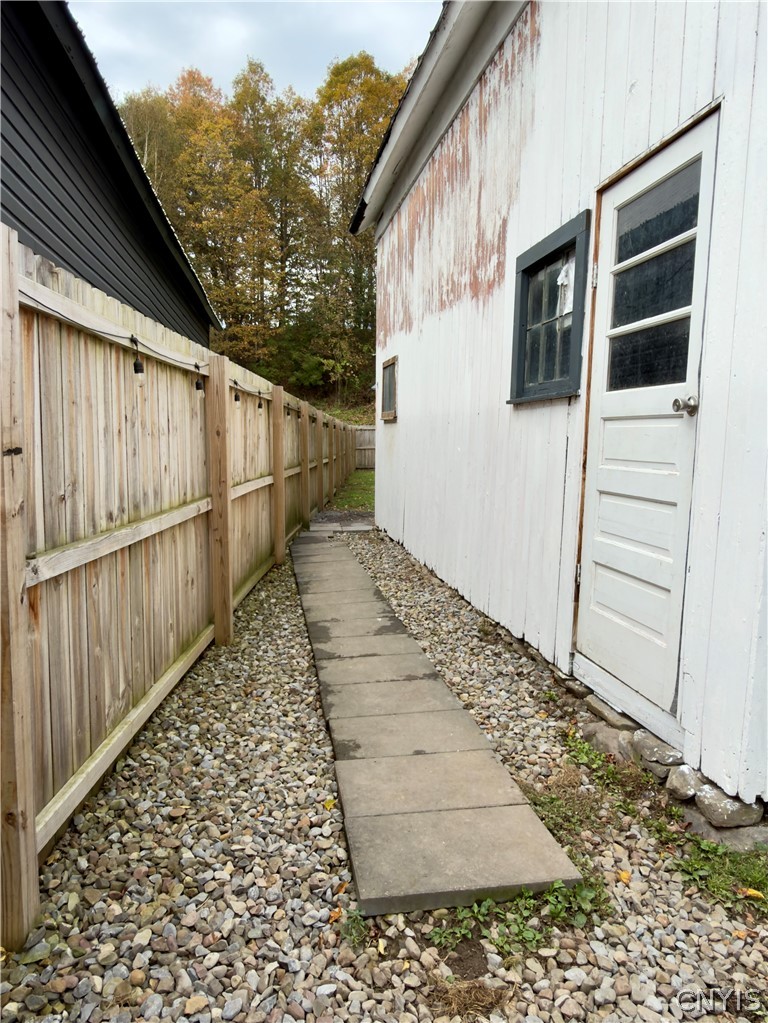 7468 Willey Road Hamilton, NY 13332 - Photo 14 of 19 A stone-paved walkway runs alongside the wood-clad exterior, bordered by a sturdy privacy fence.