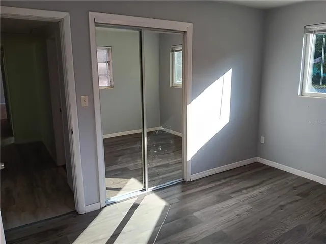 an empty room with wooden floor closet and windows