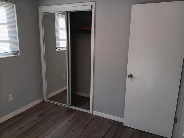 an empty room with wooden floor closet and windows