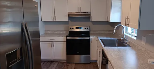 a kitchen with stainless steel appliances granite countertop a refrigerator a stove and a sink with wooden floor