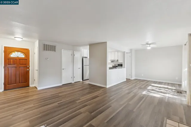a view of an empty room with wooden floor and kitchen view