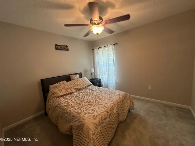 a bed sitting in a bedroom next to a window and a ceiling fan