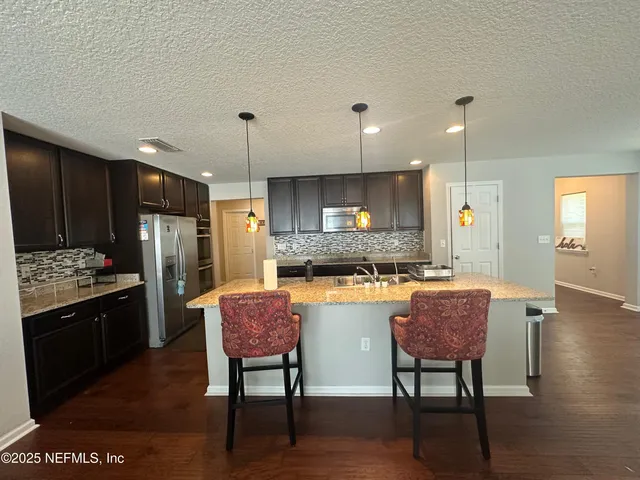 a kitchen with stainless steel appliances kitchen island granite countertop a refrigerator a stove a sink a dining table and chairs with wooden floor