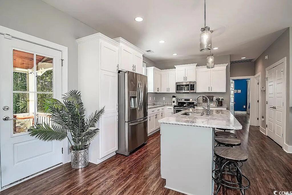 399 Lumbee Circle Pawleys Island, SC 29585 - Photo 9 of 30 Kitchen featuring appliances with stainless steel finishes, a kitchen bar, white cabinetry, dark wood-style flooring, and pendant lighting