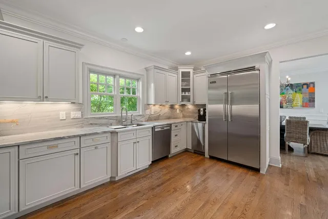 a kitchen with stainless steel appliances granite countertop a refrigerator a sink a stove and white cabinets with wooden floor