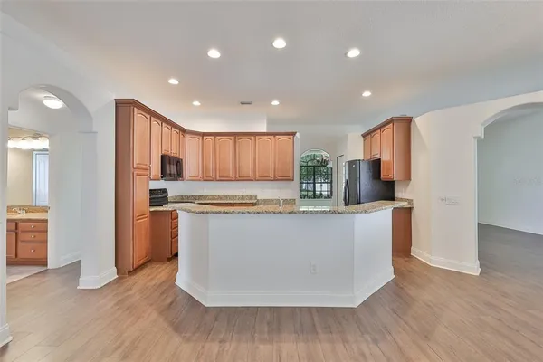 a kitchen with stainless steel appliances granite countertop a refrigerator a sink a stove a microwave and white cabinets with wooden floor