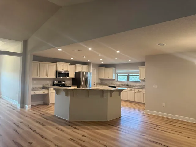 a kitchen with stainless steel appliances a stove top oven a sink a refrigerator white cabinets and wooden floor