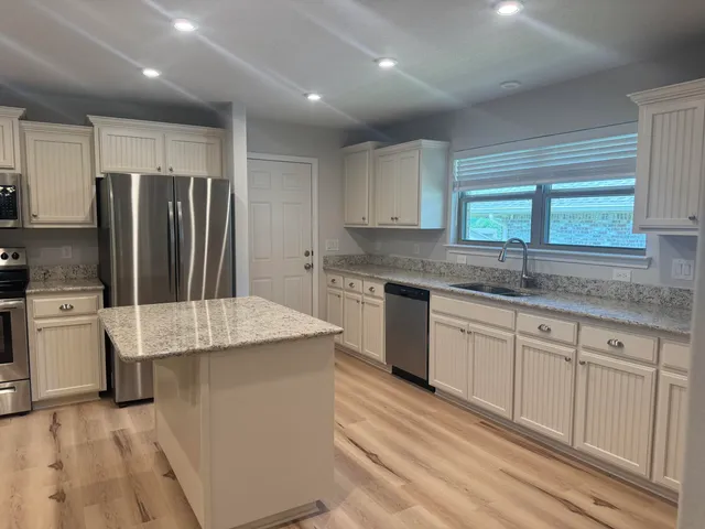 a kitchen with stainless steel appliances granite countertop a sink dishwasher a refrigerator and white cabinets with wooden floor