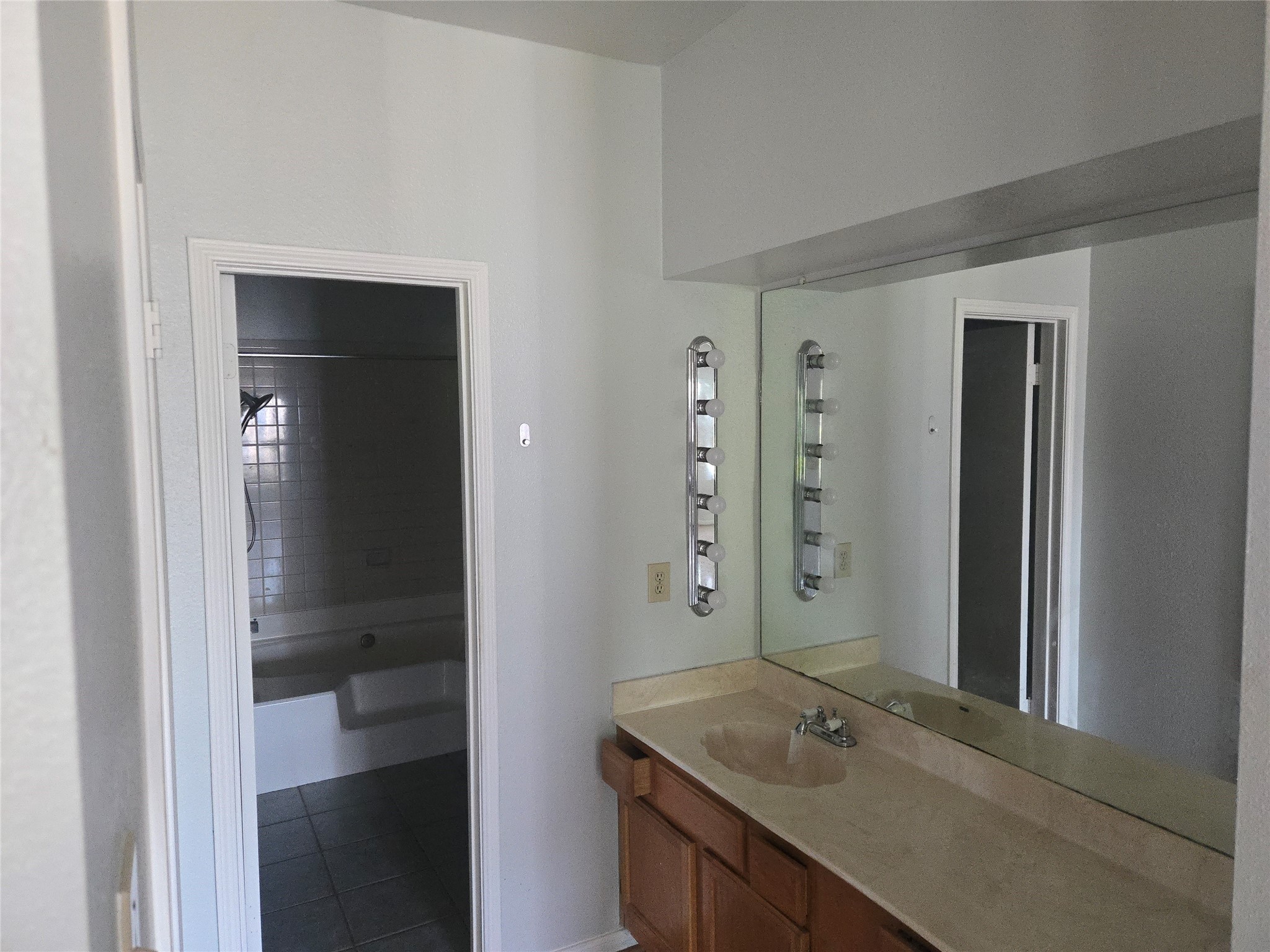 3780 Tanglewilde Street, Unit 501 Houston, TX 77063 - Photo 8 of 26 This photo shows a bathroom with a large vanity and mirror, featuring a countertop sink and ample lighting. There's a doorway leading to a separate tiled shower and bathtub area. The space offers practical functionality with a simple, clean design.