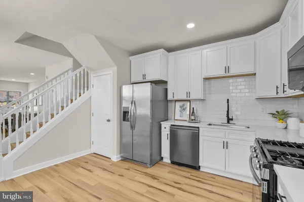 a kitchen with stainless steel appliances granite countertop a refrigerator a stove a sink dishwasher and white cabinets with wooden floor