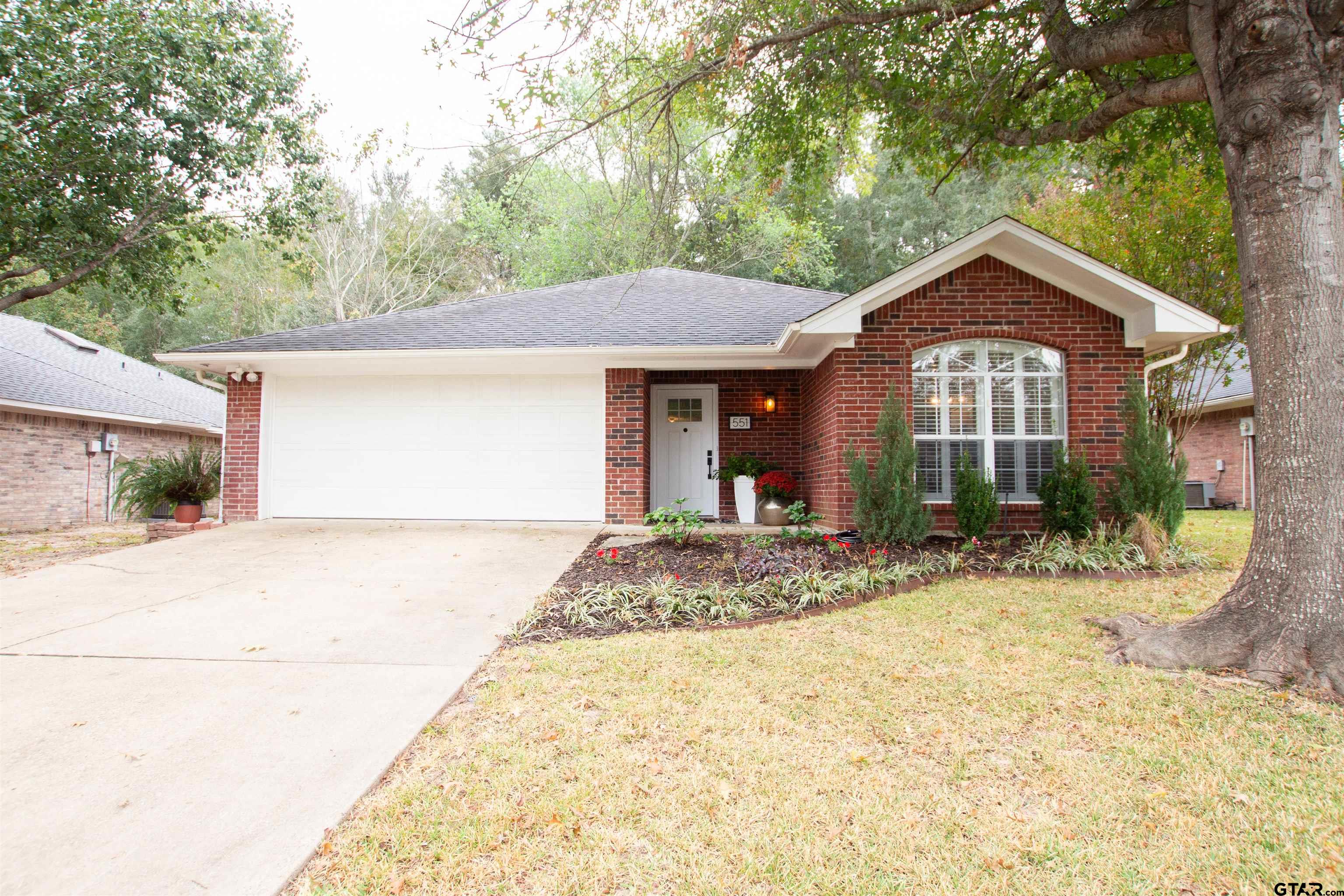 a view of a house with a yard plants and large tree