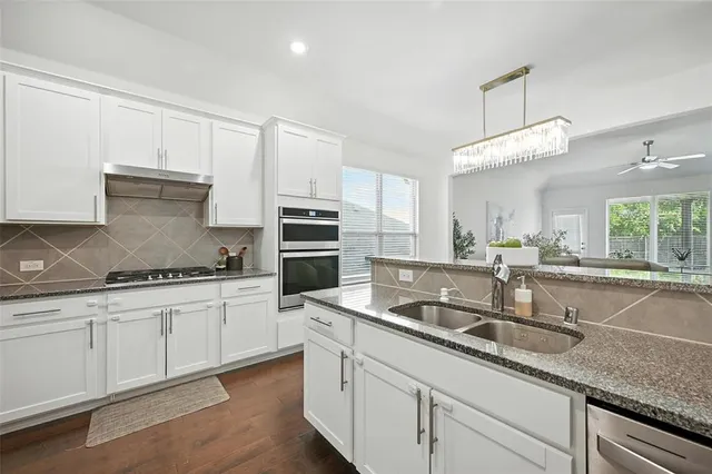 a kitchen with granite countertop a sink stainless steel appliances white cabinets and a window