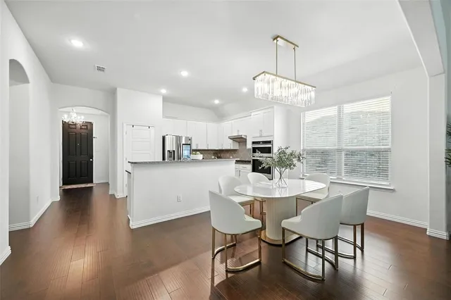 a dining room with wooden floor a chandelier a glass table and chairs