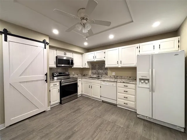 a kitchen with granite countertop a refrigerator oven a sink and white cabinets