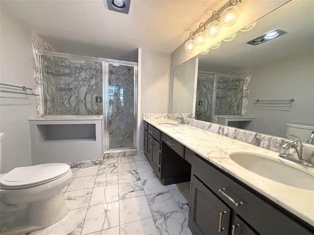 a spacious bathroom with a granite countertop sink a toilet a mirror and shower