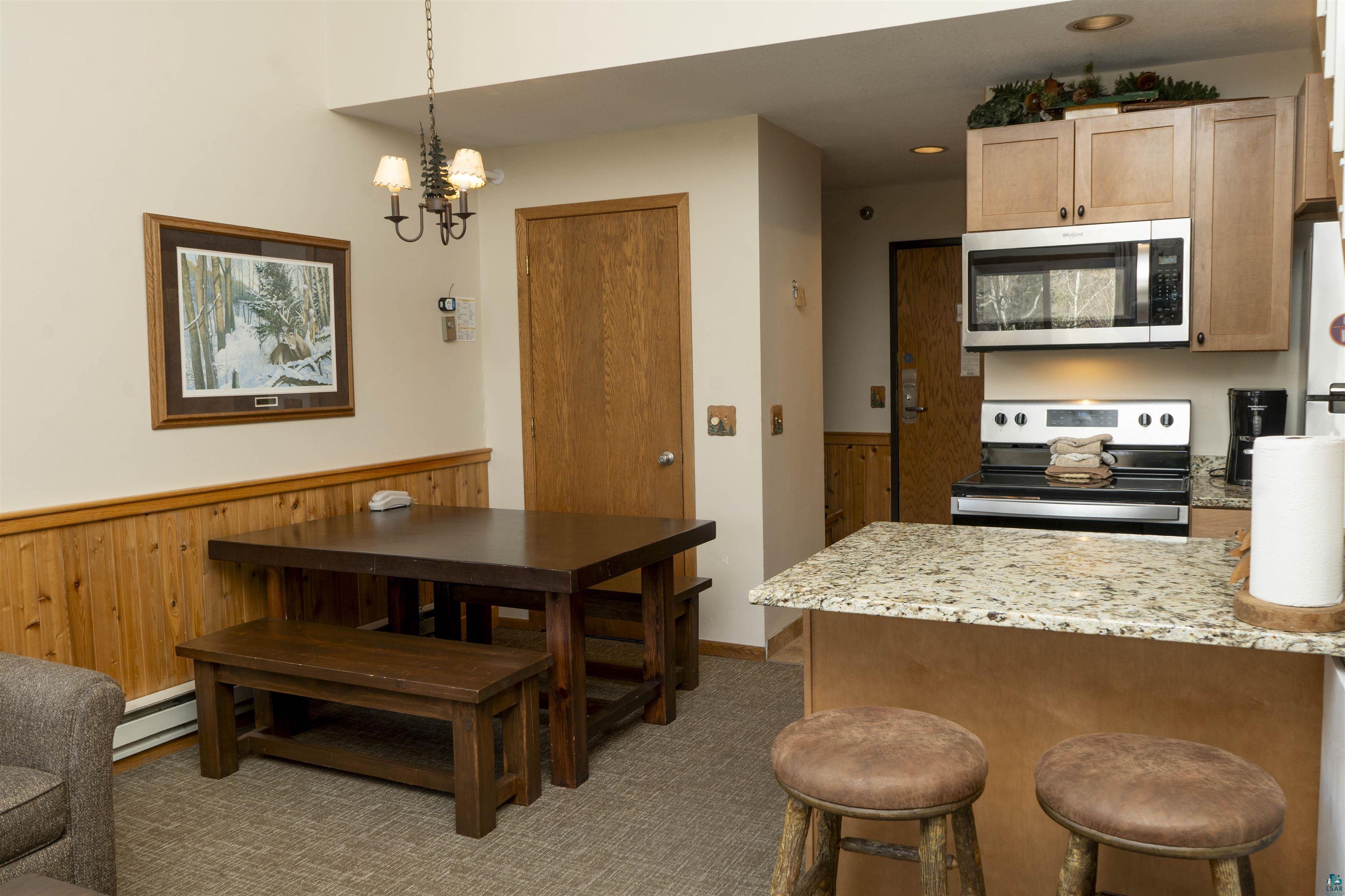 111 Bridge Run Lane, Unit 111 Lutsen, MN 55612 - Photo 11 of 48 Dining area with wood walls, a chandelier, a baseboard radiator, dark carpet, and a wainscoted wall