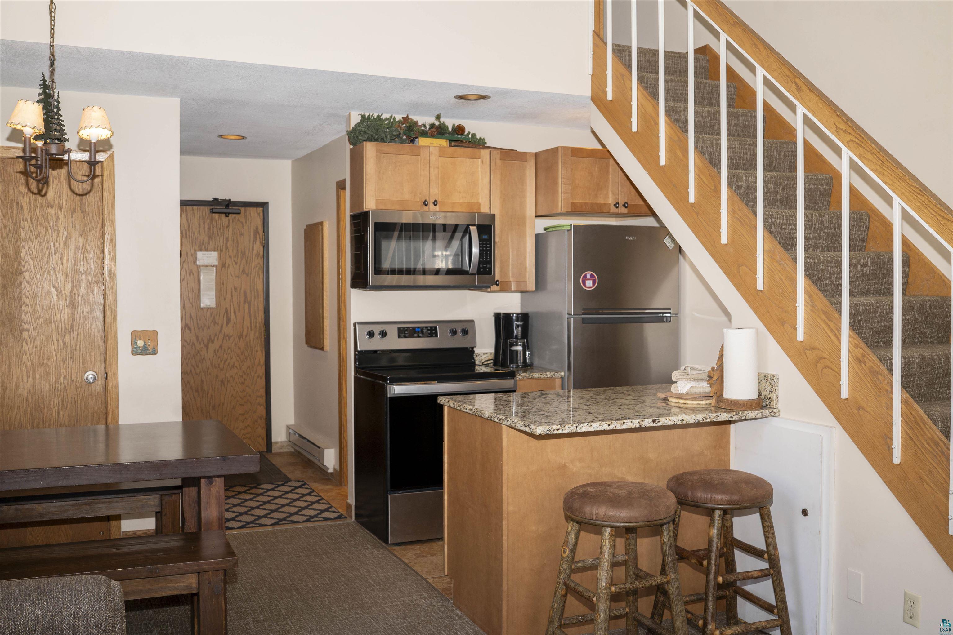 111 Bridge Run Lane, Unit 111 Lutsen, MN 55612 - Photo 3 of 48 Kitchen with appliances with stainless steel finishes, light stone countertops, pendant lighting, brown cabinets, and a breakfast bar