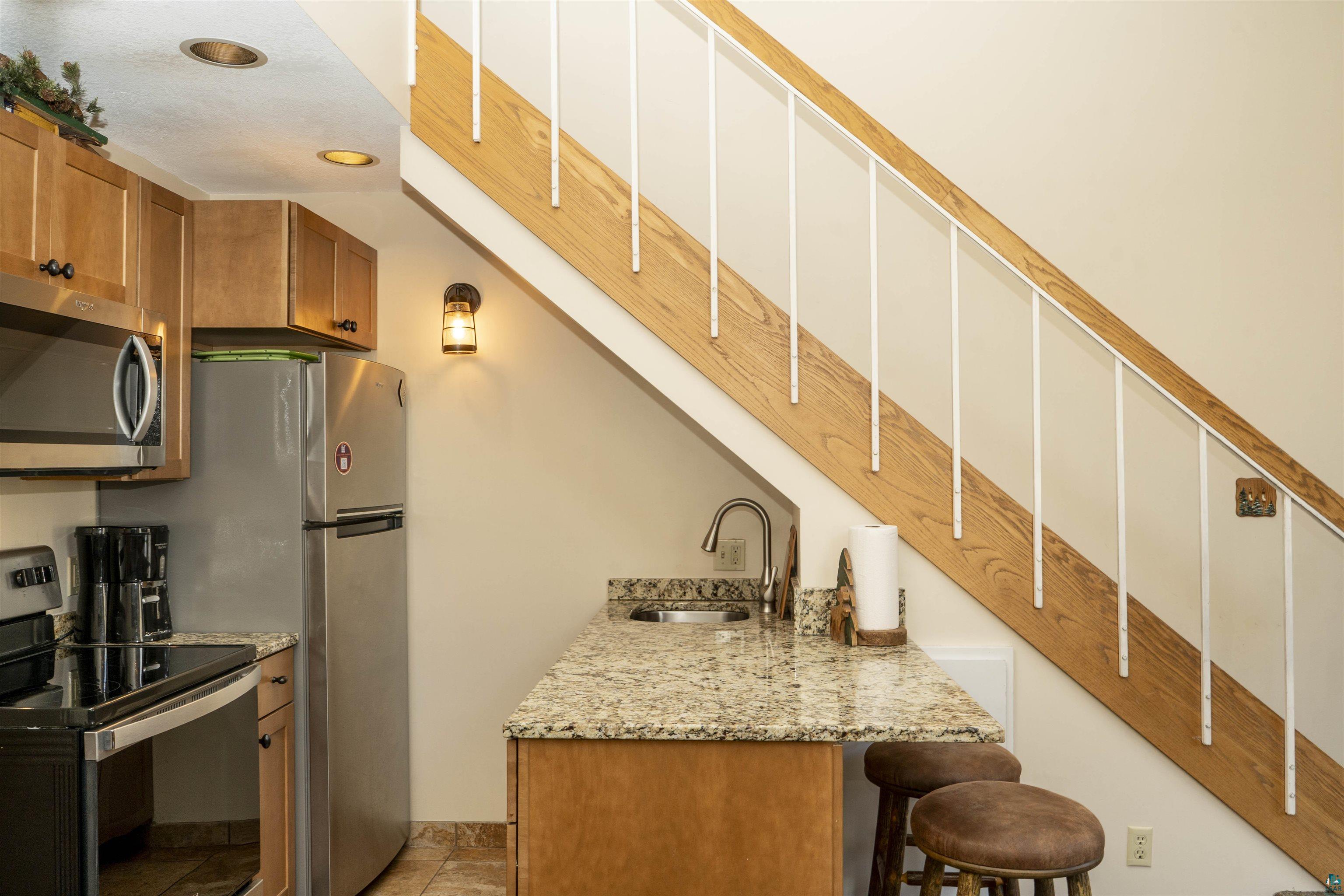 111 Bridge Run Lane, Unit 111 Lutsen, MN 55612 - Photo 8 of 48 Kitchen with appliances with stainless steel finishes, brown cabinetry, light stone counters, and a breakfast bar
