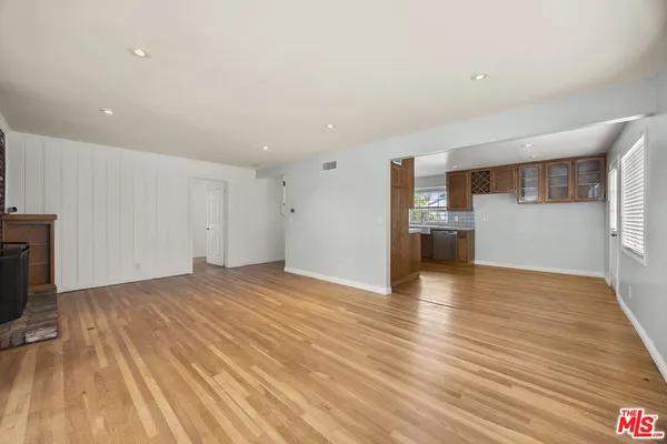a view of empty room with wooden floor and kitchen
