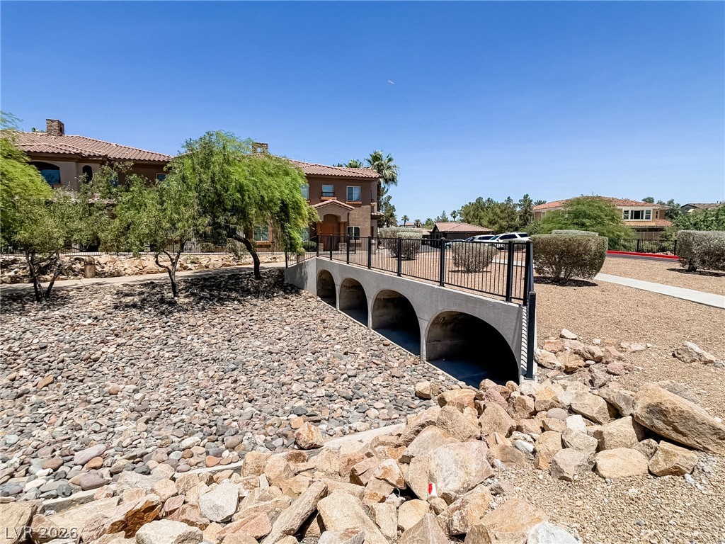 7701 West Robindale Road, Unit 110 Las Vegas, NV 89113 - Photo 20 of 21 A picturesque bridge spans a rock-filled arroyo, leading to Mediterranean-inspired residences under a clear sky.