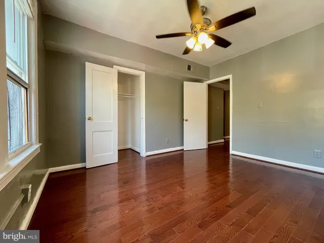 an empty room with wooden floor chandelier fan and windows