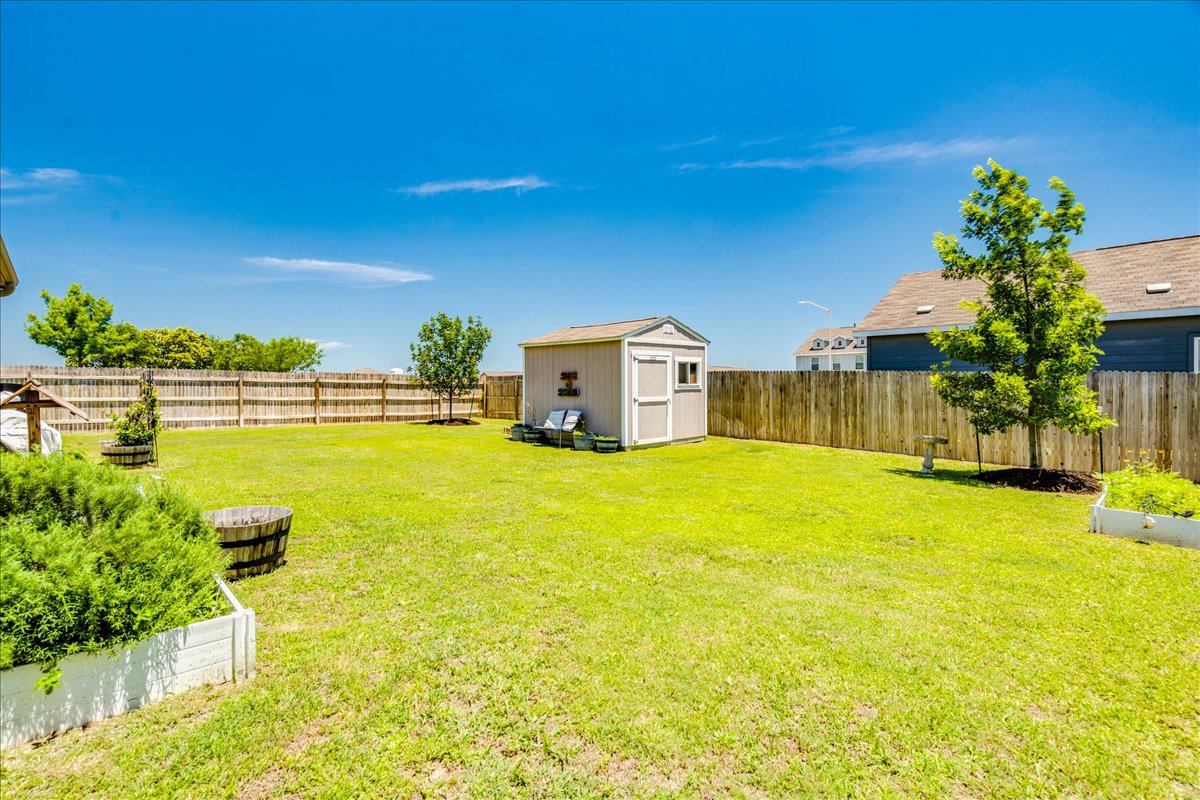 358 Jasper Trail Buda, TX 78610 - Photo 31 of 35 Expansive fenced yard featuring a storage shed, trees, and raised garden beds