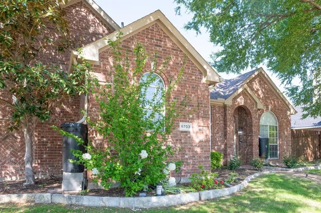 a view of a brick house with a yard plants and large tree
