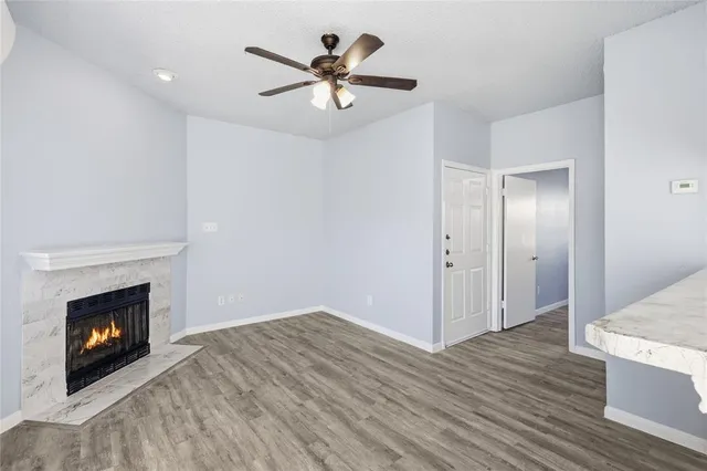 a view of an empty room with wooden floor a fireplace and a ceiling fan