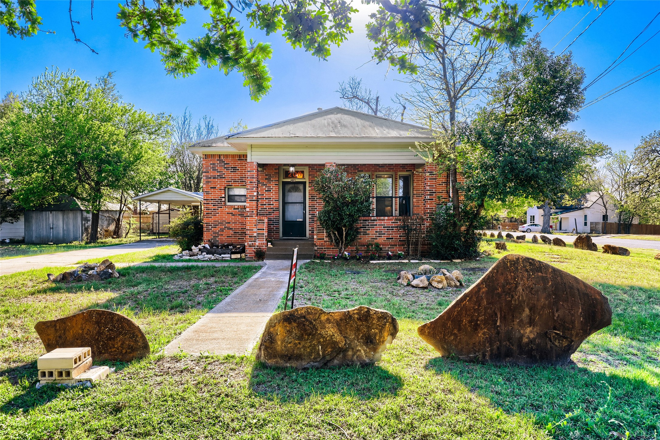208 North Ave B Elgin, TX 78621 - Photo 2 of 29 Enjoy your welcoming front porch, set on a spacious, grassy lot. Mature trees provide shade, and decorative rocks enhance the landscape.