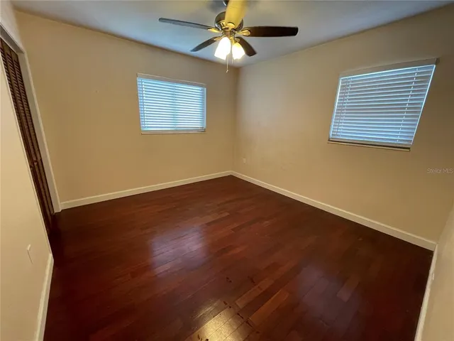 a view of an empty room with wooden floor and a chandelier fan