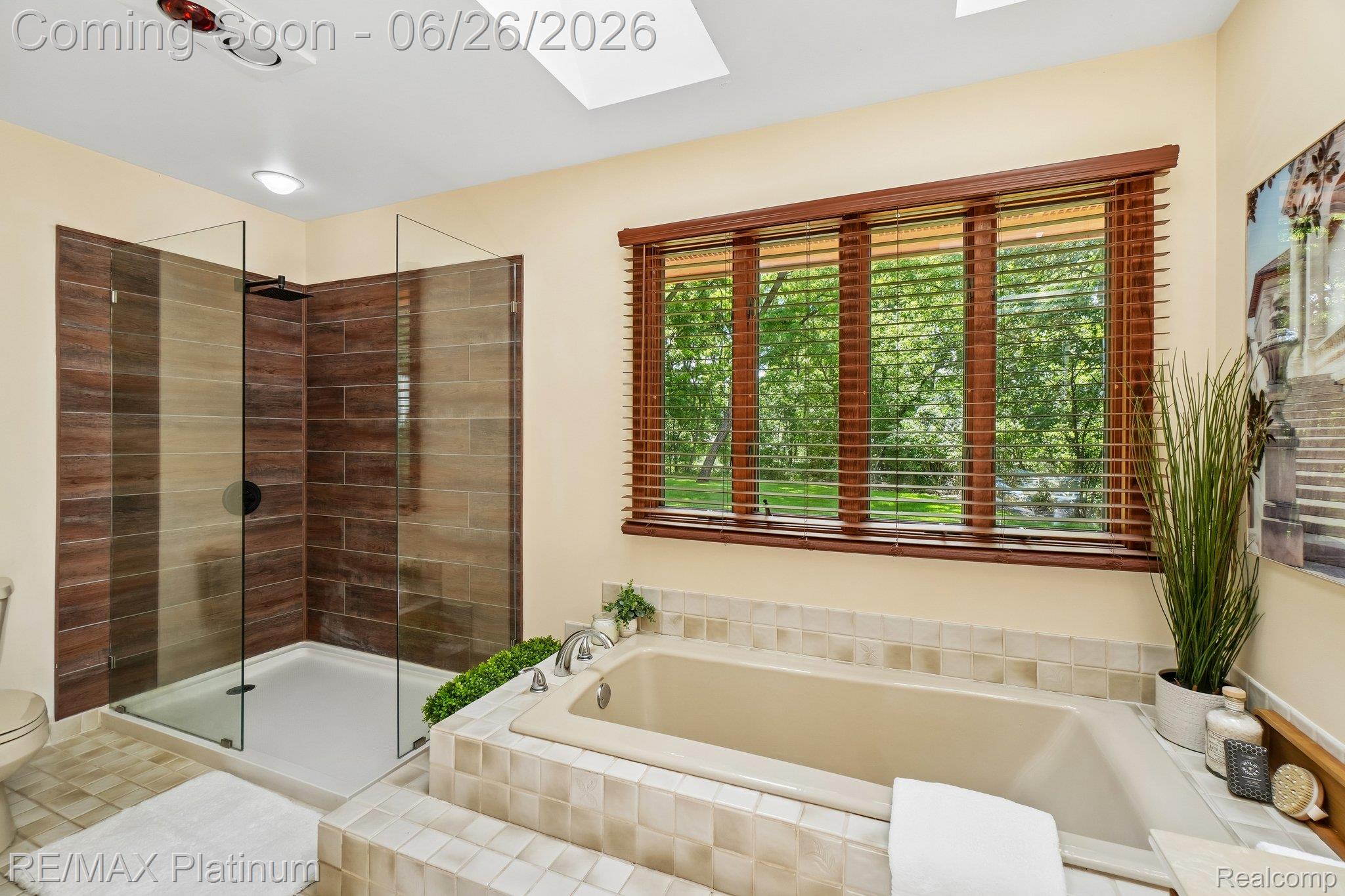 6100 Oak Valley Road Brighton, MI 48116 - Photo 20 of 47 Spacious bathroom featuring a glass-enclosed shower with wood-finish tile, an integrated bathtub with tiled surround, a large window with wood blinds, and a skylight