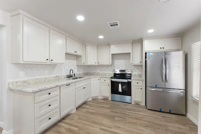 a kitchen with stainless steel appliances granite countertop a refrigerator a sink dishwasher a stove and white cabinets with wooden floor