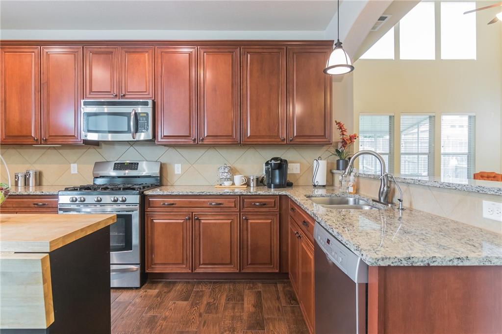 252 Pond View Pass Buda, TX 78610 - Photo 7 of 37 Kitchen with appliances with stainless steel finishes, a peninsula, light stone counters, and dark wood-style floors