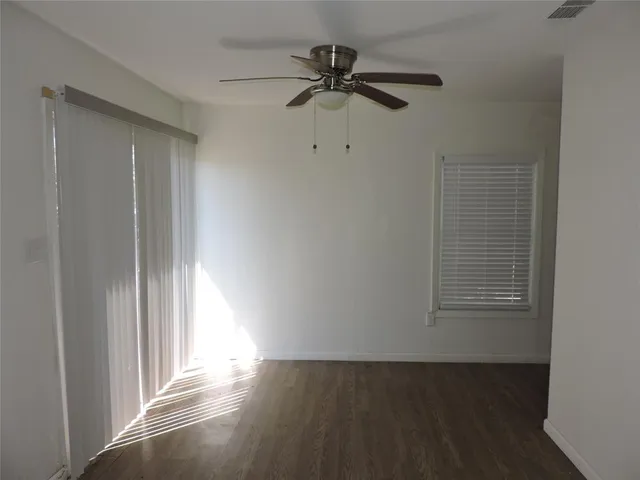 an empty room with wooden floor ceiling fan and windows