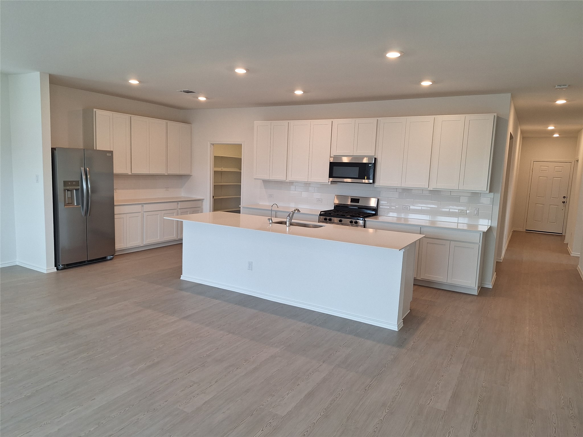 18001 Prairie Falcon Way Pflugerville, TX 78660 - Photo 36 of 38 Contemporary kitchen featuring a large central island, stainless steel appliances, white cabinetry, and light-toned flooring
