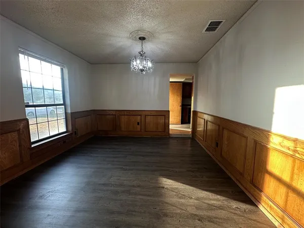 a view of an empty room with wooden floor and a kitchen