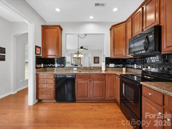 a kitchen with stainless steel appliances granite countertop a stove a sink dishwasher and a microwave oven with wooden cabinets