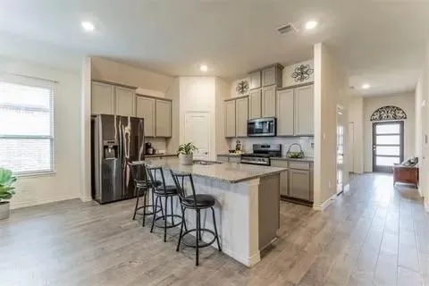 a kitchen with stainless steel appliances kitchen island granite countertop a refrigerator a stove a sink a dining table and chairs with wooden floor
