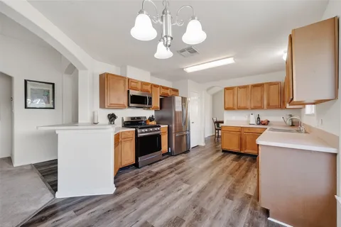 a kitchen with stainless steel appliances a stove top oven a sink dishwasher a refrigerator and a dining table with wooden floor
