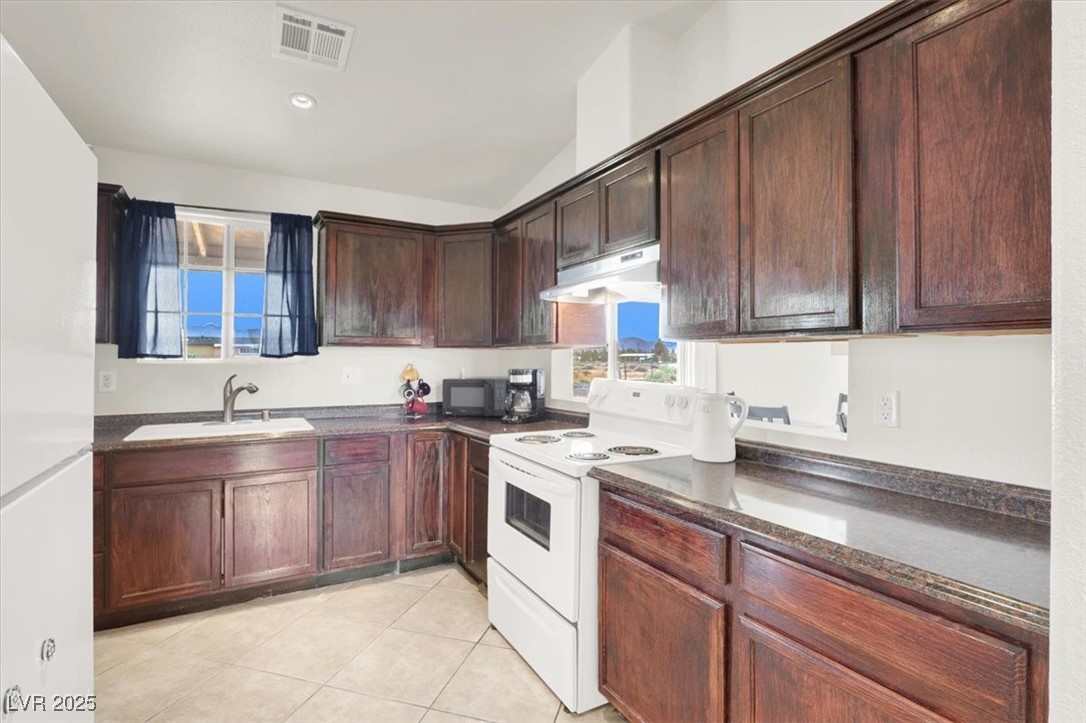 4391 Emma Street Pahrump, NV 89048 - Photo 10 of 28 Kitchen featuring white appliances, under cabinet range hood, light tile patterned floors, dark brown cabinets, and dark stone counters
