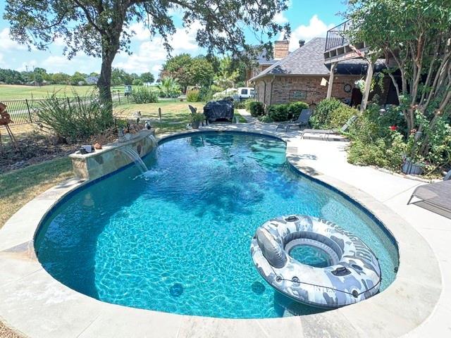 1762 Timber Ridge Circle Corinth, TX 76210 - Photo 22 of 26 Freeform swimming pool with integrated stone waterfall feature, concrete pool decking, and mature landscaping
