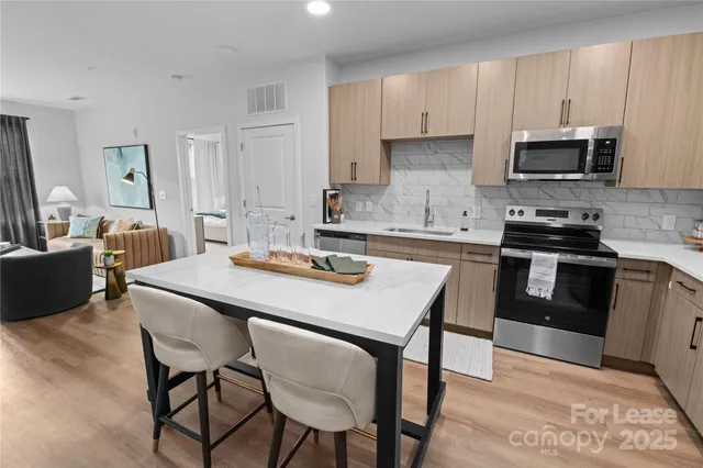 a kitchen with stainless steel appliances a table chairs sink and cabinets