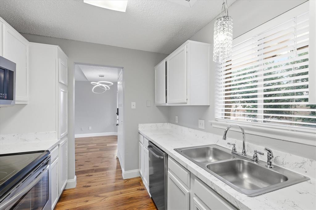 5550 Spring Valley Road, Unit A31 Dallas, TX 75254 - Photo 7 of 24 Galley-style kitchen featuring white cabinetry, light-toned countertops, a dual-basin stainless steel sink with a chrome faucet, and wood-finish flooring